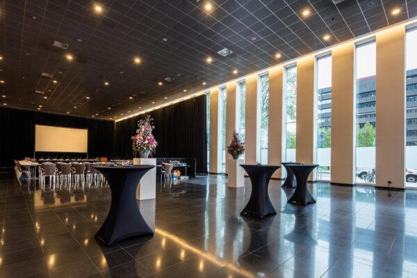 Moderne vergaderzaal aan de Prinses Beatrixlaan met grote ramen, bloemstukken en statafels.